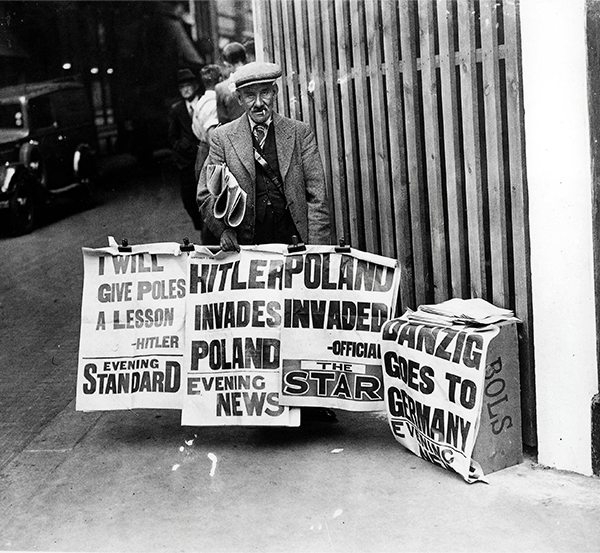 black and white photo of a man holding newspaper headlines about World War II